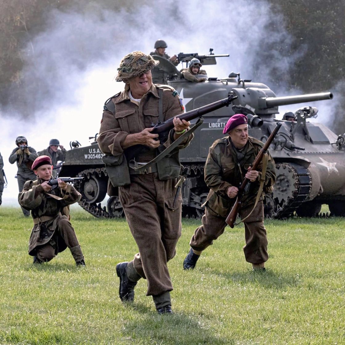 Living History reenactors in WWII uniforms advancing past a Sherman tank